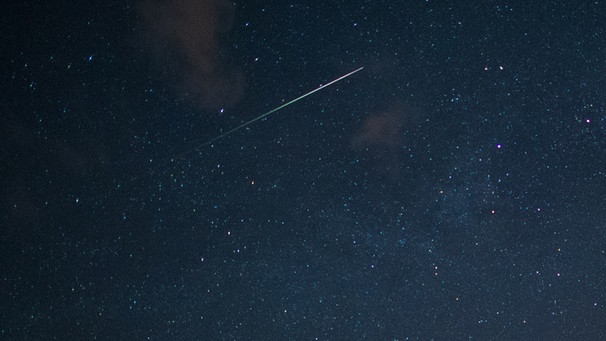 Eine Sternschnuppe fliegt über den dunklen Nachthimmel. | Bild: picture-alliance/dpa