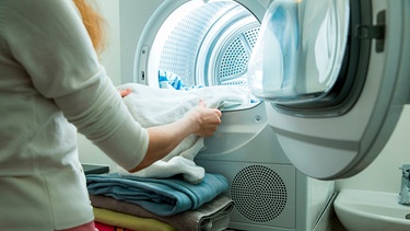 Person nimmt Wäsche aus einem Wäschetrockner | Bild: mauritius images  Aleksandra Suzi  Alamy  Alamy Stock Photos