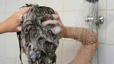 Eine Frau wäscht ihre Haare mit Shampoo.  | Bild: picture-alliance/ ZB | Patrick Pleul