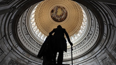 Die Kuppel des Kapitols in Washington, in dem der US-Kongress seinen Sitz hat, davor eine Statue, die den ersten US-Präsidenten George Washington mit einem Schwert zeigt. | Bild: picture-alliance/dpa