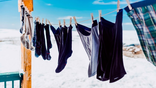 In einem schneebedeckten Garten hängt Wollwäsche an einer Wäscheleine. | Bild: mauritius-images