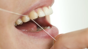 Eine Frau benutzt Zahnseide.  | Bild: mauritius-images