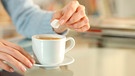 Finger einer Frau halten einen Zuckerwürfel über eine Kaffeetasse | Bild: mauritius images / Antonio Guillem / Alamy / Alamy Stock Photos