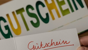 Eine Karte mit der Aufschrift "Gutschein" vor einer gedruckten Karte. | Bild: picture alliance/dpa | Swen Pförtner