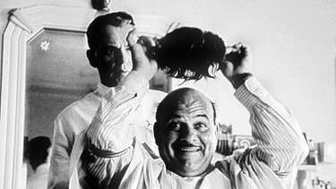 Screenshot aus dem Schwarz-Weiß-Film "The Man who wasn't there" mit Billy Bob Thornton, der hier als Friseur einem glatzköpfigen Kunden ein Toupet aufsetzt. | Bild: picture-alliance/dpa