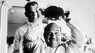 Screenshot aus dem Schwarz-Weiß-Film "The Man who wasn't there" mit Billy Bob Thornton, der hier als Friseur einem glatzköpfigen Kunden ein Toupet aufsetzt. | Bild: picture-alliance/dpa