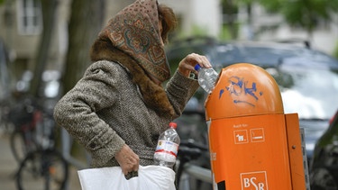 Eine alte Frau sucht in einem Abfalleimer nach Pfandflaschen. | Bild: picture-alliance/dpa