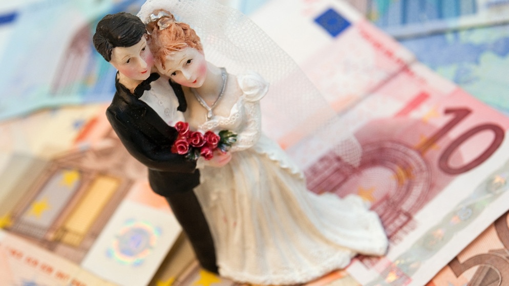 ILLUSTRATION - Die Figuren eines Hochzeitspaares stehen auf Geldscheinen. | Bild: picture alliance / dpa Themendienst | Andrea Warnecke