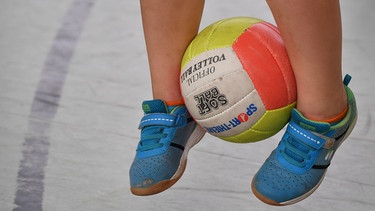 Ein Kind springt mit einem Ball zwischen den Beinen in die Luft | Bild: picture-alliance/dpa