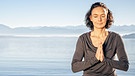 Frau meditiert am Seeufer | Bild: picture-alliance/dpa
