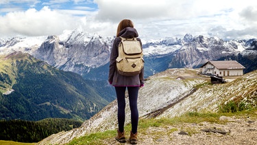 Eine Wanderin mit Rucksack auf dem Rücken schaut auf Berggipfel am Horizont | Bild: colourbox.com