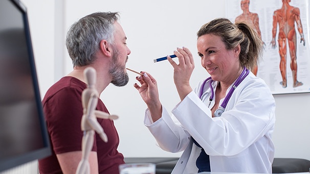 Eine Hausärztin schaut ihrem Patienten mithilfe eines Zungenspatels in den Mund. | Bild: picture-alliance/dpa