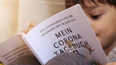 Ein Kind blättert in einem Corona-Tagebuch | Bild: picture-alliance/dpa