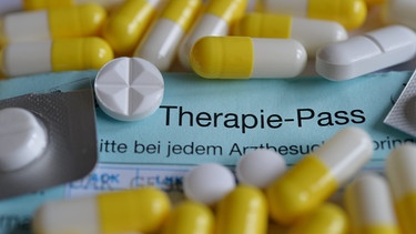 Symbolfoto: Ein Therapiepass ist zu sehen, darauf verteilt unterschiedliche Tabletten. | Bild: picture-alliance/dpa