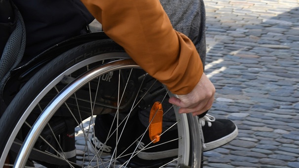 Blick von der Seite auf die Hand eines Rollstuhlfahrer, die das Laufrad über ein Kopfsteinpflaster schiebt. | Bild: picture-alliance/dpa