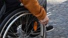 Blick von der Seite auf die Hand eines Rollstuhlfahrer, die das Laufrad über ein Kopfsteinpflaster schiebt. | Bild: picture-alliance/dpa