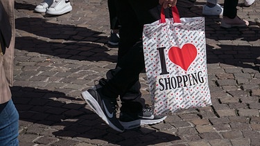Ein Mann trägt eine Plastiktüte mit der Aufschrift "I love shoppig". | Bild: picture alliance/dpa | Frank Rumpenhorst