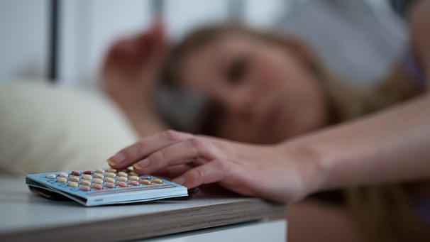 Frau im Bett greift nach Pillenschachtel. | Bild: picture-alliance/dpa
