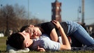 Auf der Wiese liegend genießt ein junges Paar die warmen Strahlen der Frühlingssonne.  | Bild: dpa-Bildfunk/Wolfgang Kumm