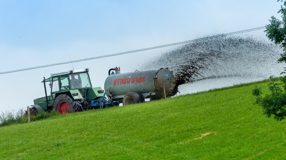 Ein Traktor zieht eine Landwirtschaftsmaschine, mit der Gülle auf ein gemähtes Feld verteilt wird. | Bild: Peter Kneffel/dpa +++ dpa-Bildfunk +++