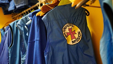 An einer Garderobe hängen Westen - versehen mit dem Logo der Bahnhofsmission. | Bild: picture-alliance/dpa