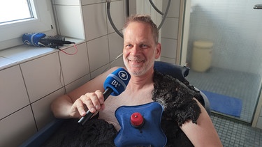 Reporter Chris Baumann entspannt im Moorbad mit Torf und beim Interview. Auf der Brust liegt der Herzkühler. | Bild: BR / Chris Baumann