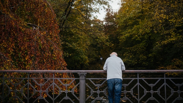 Ein alter Mann lehnt an einer Brücke im Park. | Bild: BR/Julia Müller