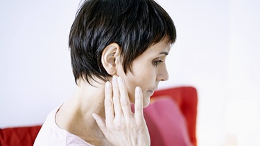 Eine Frau hält sich die Hand ans rechte Ohr, weil sie irgendetwas zu irritieren scheint. | Bild: picture-alliance/dpa