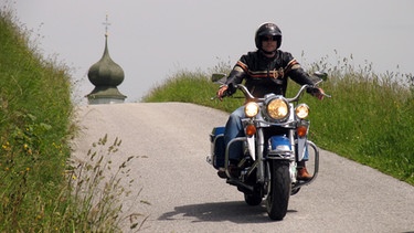 Ein Mann fährt eine Harley Davidson, im Hintergrund eine Kirchturmspitze | Bild: picture-alliance/dpa
