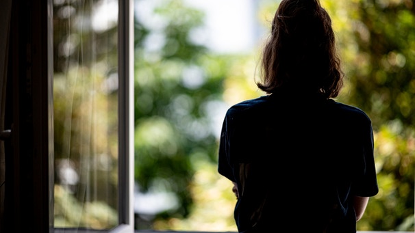 Eine junge Frau steht in ihrer Wohnung an einem Fenster. | Bild: dpa-Bildfunk/Fabian Sommer