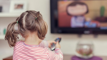 Ein Mädchen wechselt den Fernsehkanal mit der Fernbedienung. | Bild: stock.adobe.com/Myst