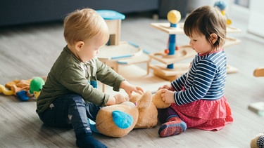Zwei Kinder spielen zusammen auf dem Boden. | Bild: stock.adobe.com/very_ulissa