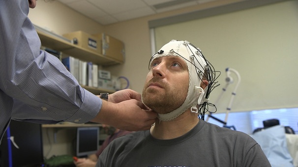 Ein ME/CFS sitzt mit einer EEG-Haube im Labor. | Bild: picture-alliance/dpa, AP Photo