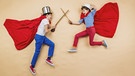 Zwei Kinder mit Umhängen kämpfen superman-like mit Kochlöffeln gegeneinander. Dabei liegen sie seitlich auf dem Boden und werden von oben fotografiert, sodass es aussieht, als flögen sie mit gezückten "Schwertern" aufeinander zu. | Bild: www.colourbox.de