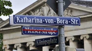 Das Straßenschild Meiserstraße ist mit rotem Klebeband abgedeckt, darüber hängt am Donnerstag (27.05.2010) in München das neue Straßenschild Katharina-von-Bora-Straße. Im Hintergrund der Königsplatz.  | Bild: picture-alliance/dpa
