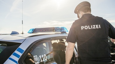 Symbol: Ein Polizist neben einem Polizeiauto | Bild: BR/Fabian Stoffers