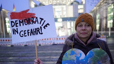 Eine Demonstrantin mit einem Schild "Demokratie in Gefahr", 12. Januar 2024, Berlin. Demonstration unter dem Motto "AfD Verbot prüfen - jetzt!" vor dem Bundeskanzleramt | Bild: Joerg Carstensen/dpa +++ dpa-Bildfunk +++