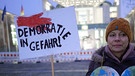 Eine Demonstrantin mit einem Schild "Demokratie in Gefahr", 12. Januar 2024, Berlin. Demonstration unter dem Motto "AfD Verbot prüfen - jetzt!" vor dem Bundeskanzleramt | Bild: Joerg Carstensen/dpa +++ dpa-Bildfunk +++