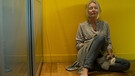 Eine barfüßige Frau sitzt erschöpft und depressiv vor einer gelben Wand und hat die Augen geschlossen. | Bild: picture-alliance/dpa
