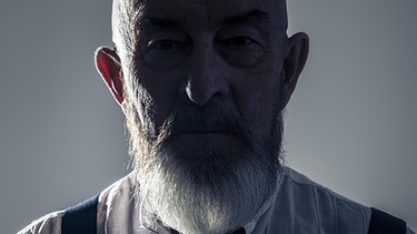 Älterer Mann mit Bart, der düster dreinschaut und dessen Gesicht im Schatten liegt. | Bild: picture-alliance/dpa