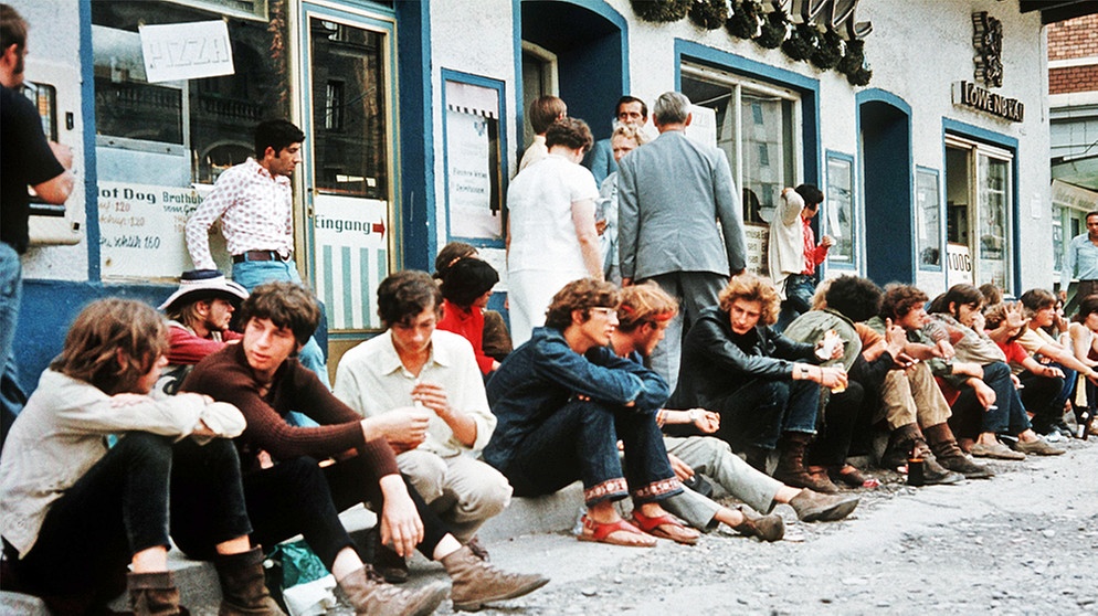 "Gammler" sitzen auf dem Bürgersteig vor dem "Picnic", einem beliebten Treffpunkt der Gammler- und Hippieszene in der Leopoldstraße der sechziger Jahre | Bild: picture-alliance/dpa