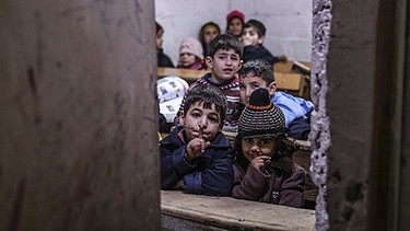 Syrische Kinder, in einem Klassenzimmer in der Nähe von Damaskus, sie blicken durch einen Spalt in der Wand | Bild: picture-alliance/dpa