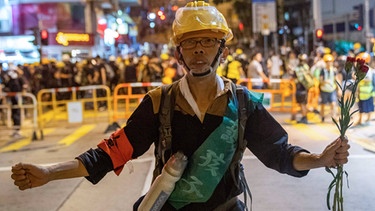 21.07.2019, China, Hongkong: Ein Demonstrant hält Blumen vor die Polizei, um ihren Vormarsch auf die Demonstranten zu verlangsamen. Bei einem neuen Massenprotest in Hongkong haben wieder Hunderttausende Menschen demonstriert. | Bild: dpa-Bildfunk/Geovien So