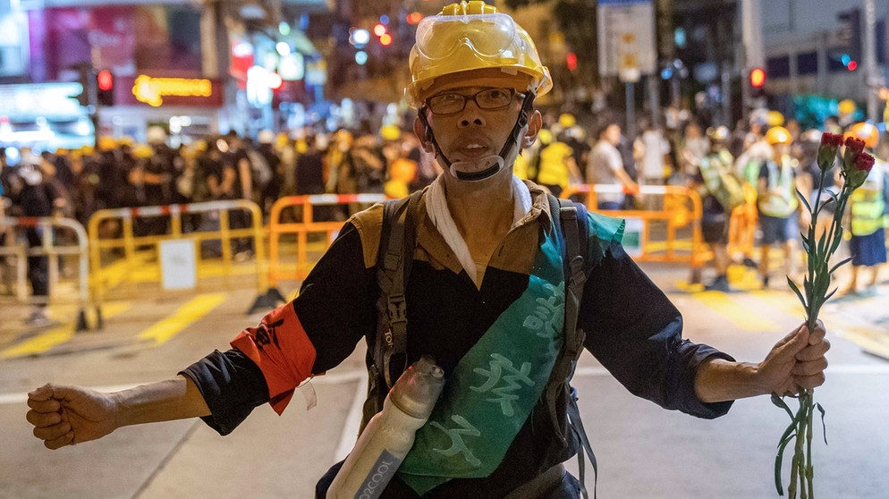 21.07.2019, China, Hongkong: Ein Demonstrant hält Blumen vor die Polizei, um ihren Vormarsch auf die Demonstranten zu verlangsamen. Bei einem neuen Massenprotest in Hongkong haben wieder Hunderttausende Menschen demonstriert. | Bild: dpa-Bildfunk/Geovien So
