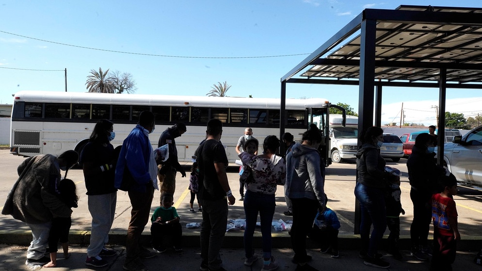 Migranten stehen im Mai 2021 vor einer Gemeinschatsunterkunft in Laredo, Texas, Schlange. Zuvor sind sie aus einem Grenzkontroll-Bus ausgestiegen. | Bild: picture alliance / ZUMAPRESS.com | John Lamparski