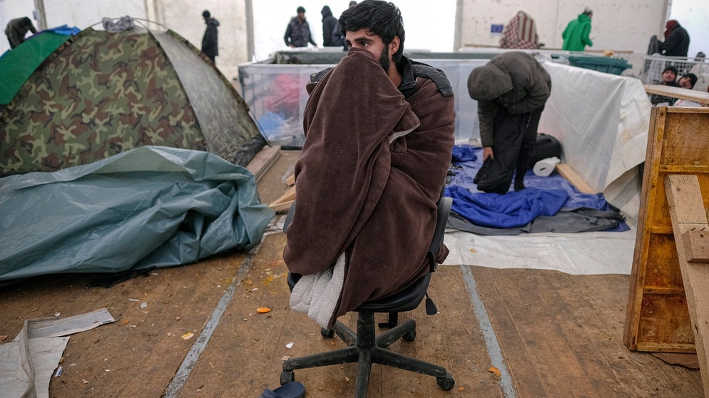 Ein Migrant aus dem Aufnahmelager Lipa sitzt in einer provisorischen Unterkunft in eine Decke gewickelt auf einem Stuhl. Die Internationale Organisation für Migration (IOM) hat am 23.12.2020 das Lager Lipa geschlossen. | Bild: dpa-Bildfunk/Kemal Softic