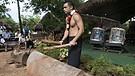 Ein Mann mit nacktem Oberkörper steht vor einer polynesischen Holztrommerl, hinter ihm ein Mann im Bastrock vor einem Mikrofon | Bild: picture-alliance/dpa
