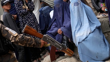 Afghanistan, Kabul: Ein Taliban-Kämpfer hält im Mai 2022 sein Gewehr in der Hand, während Menschen in Kabul auf die Verteilung von Lebensmittelrationen durch eine Hilfsorganisation warten.  | Bild: dpa-Bildfunk/Ebrahim Noroozi