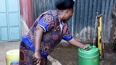 Frau füllt Wasser in Kanister an einem öffentlichen Brunnen in Nairobi | Bild: picture alliance / Mika Schmidt