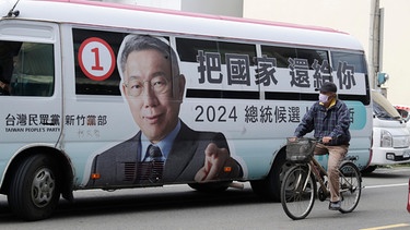 Ein Mann radelt an einem Bus mit dem Konterfei des Präsidentschaftskandidaten der Taiwanischen Volkspartei (TPP) Ko vorbei | Bild: dpa-Bildfunk/ChiangYing-ying
